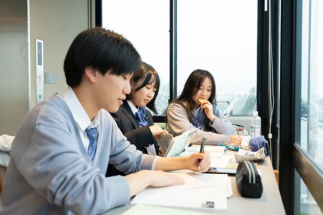 明るい窓辺の自習スペースに並び、熱心に勉強をしたりおやつを食べたりして過ごす学生たち