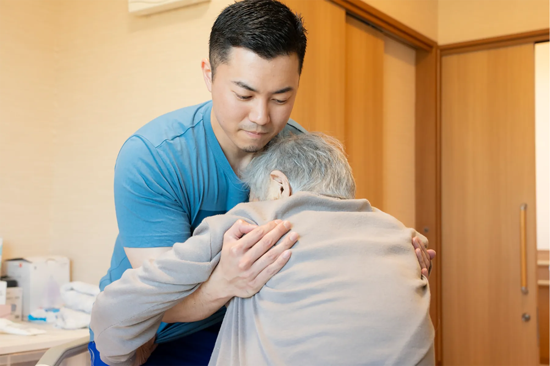 利用者の体に優しく腕を添え、真剣な表情で立ち上がりをサポートするスタッフ