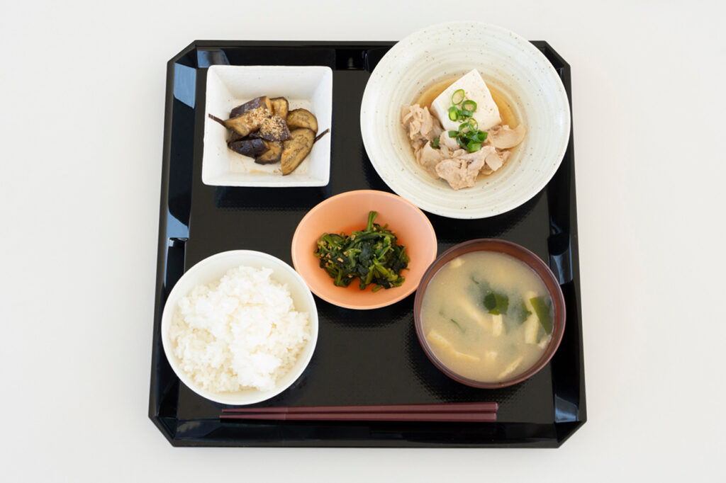 黒いお盆に載せられた、白ご飯、お味噌汁、肉豆腐、ほうれん草の和え物、ナスの煮浸しの定食