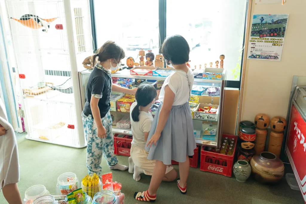 駄菓子屋の棚に並ぶたくさんのお菓子を、どれにしようか嬉しそうに選ぶ子どもたちの後ろ姿
