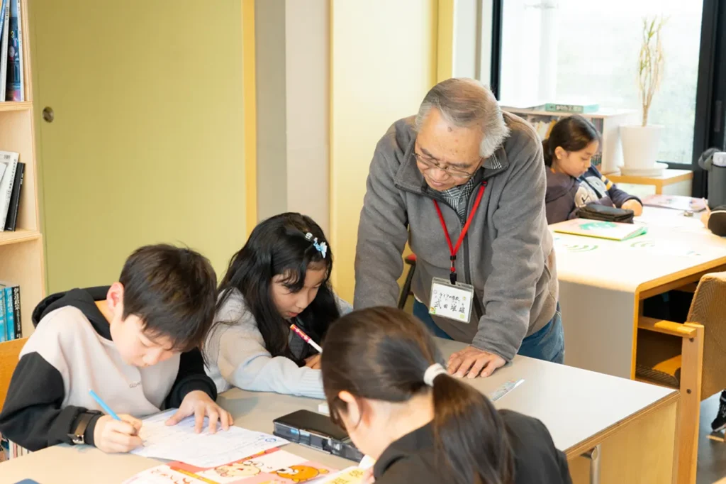 学習支援室で、ボランティアの男性が机に寄り添いながら熱心に勉強を教える学習支援の様子