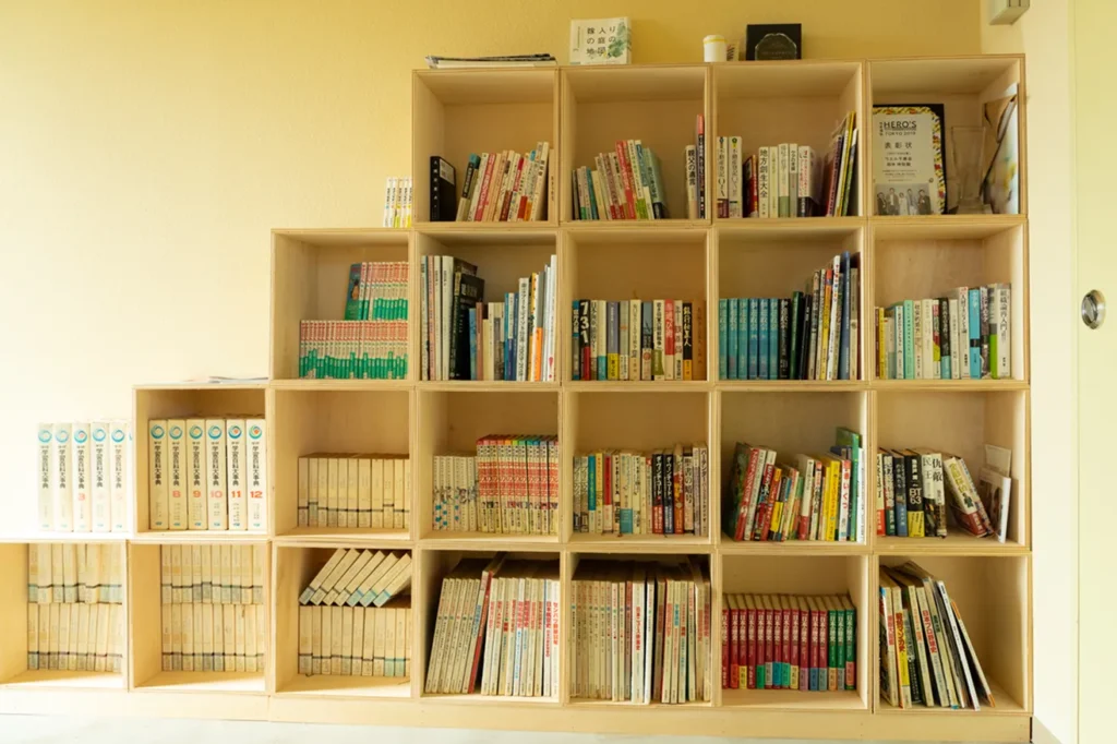 壁一面の木製ラックに、様々なジャンルの書籍や図鑑がぎっしりと並ぶ温かみのある書棚