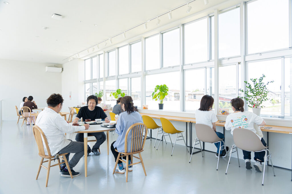 大きな窓から自然光が降り注ぐ広々とした空間で、食事や自習を思い思いに楽しむ地域の人々