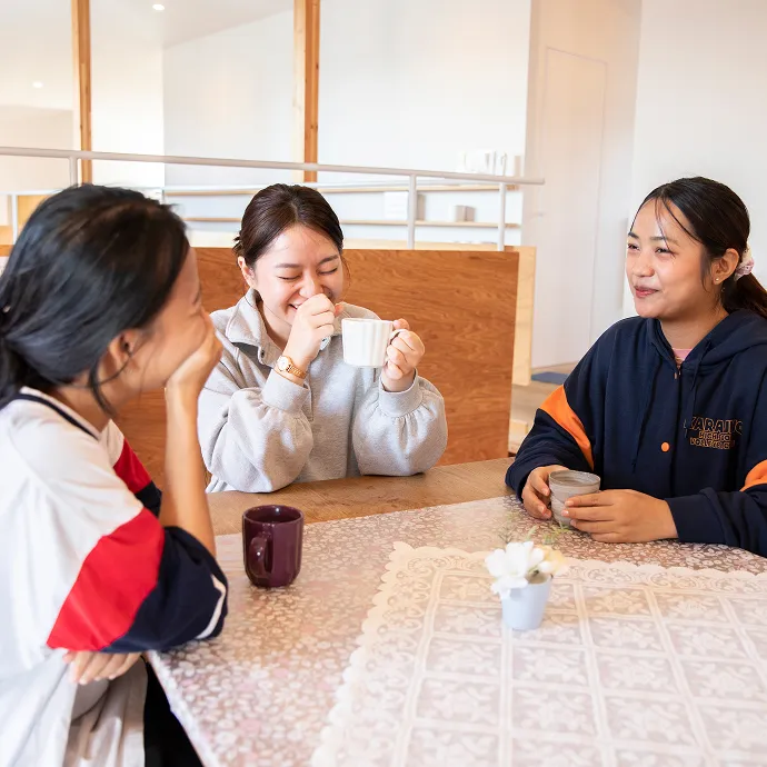 アットホームな談話スペースで、テーブルを囲みながら笑顔で楽しそうに語り合う若い女性たち