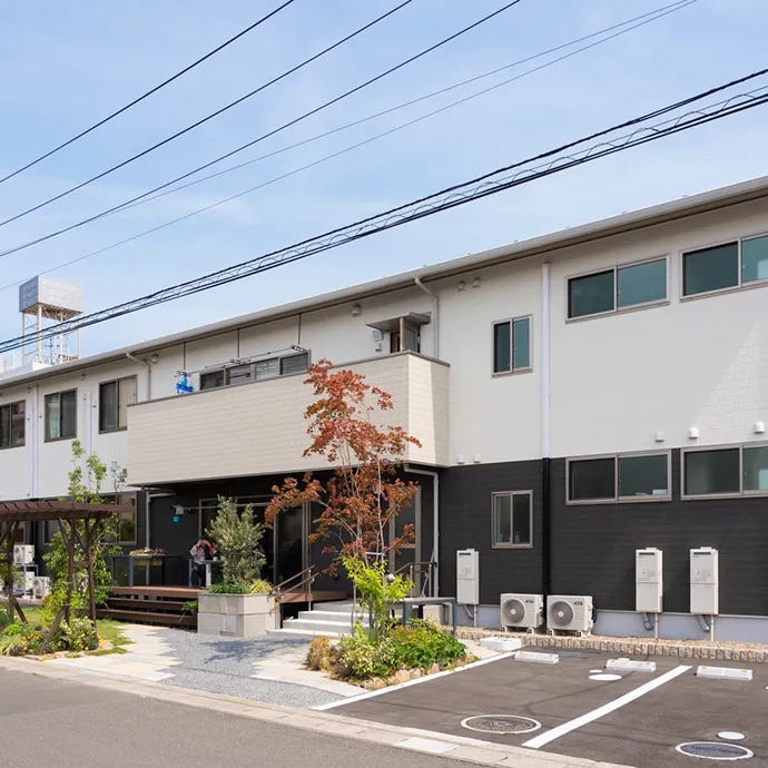 青空のもと、シックな2トーンカラーの壁面と手前の緑豊かな植栽が調和する「幸町キャンパス」の建物外観