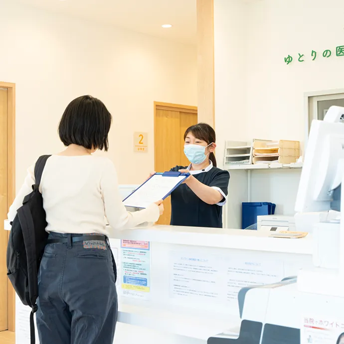 明るく清潔な受付カウンターで、来院した患者へ笑顔で丁寧に問診票を手渡すマスク姿のスタッフ